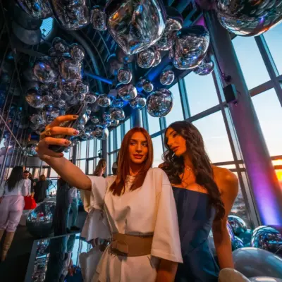 Guests taking a selfie at the Belgrade 360 Deck VIP opening with a panoramic view of Belgrade at sunset.