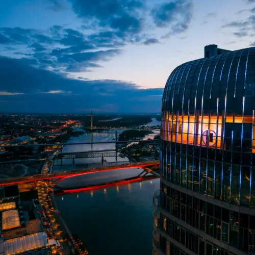 Panoramski pogled na Belgrade 360 Deck u Kuli Beograd pri zalasku sunca, sa rekom Savom, mostovima i osvetljenim gradom u pozadini.